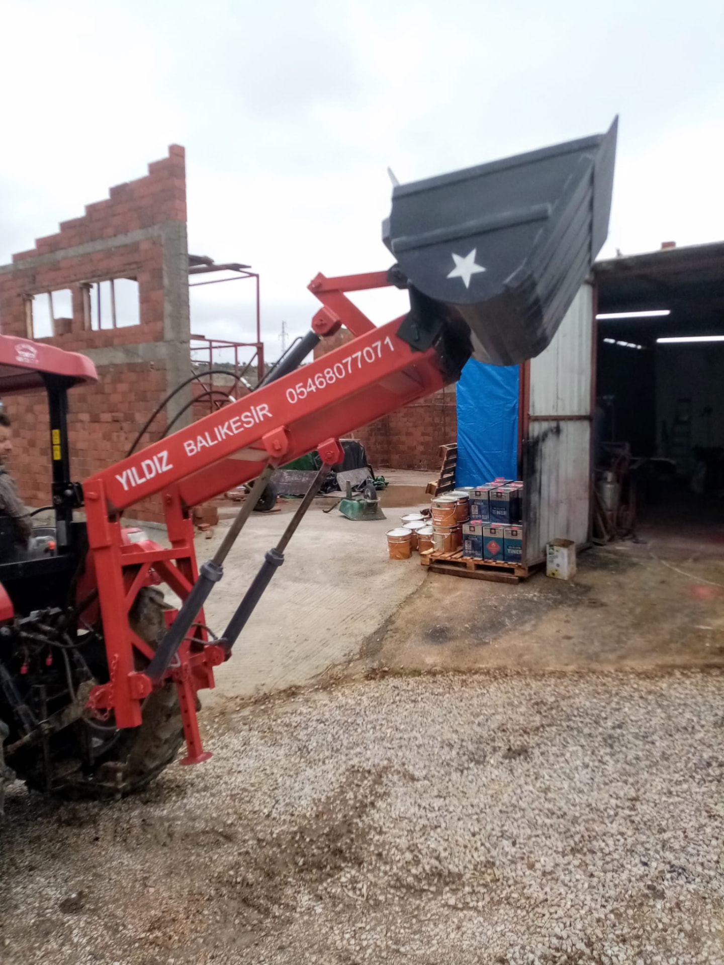 Traktöre monte edilmiş kırmızı ön yükleyici kolu ve kaldırılmış gri çelik kepçe
