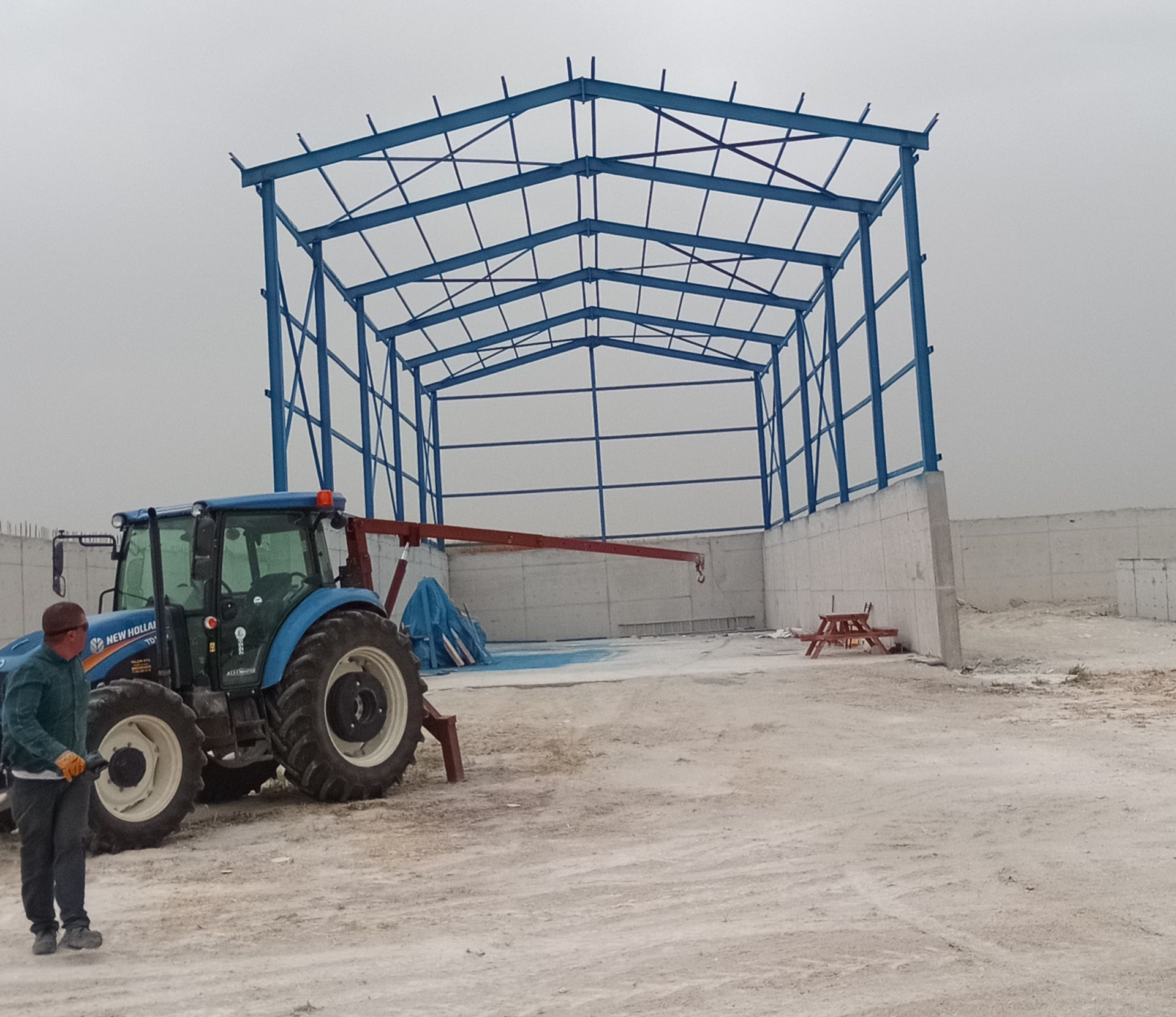 Beton duvarlar üzerinde yükselen mavi çelik kolon, çatı makası ve çaprazlardan oluşan depo iskeleti