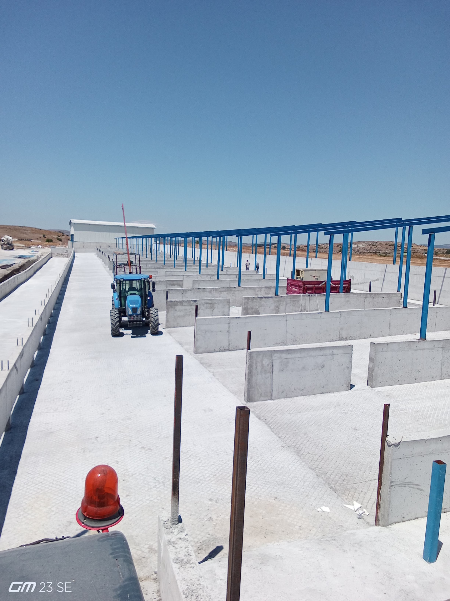 Beton bölmeli tesiste sıralanmış mavi çelik kolon ve kirişlerden oluşan gölgelik iskeleti