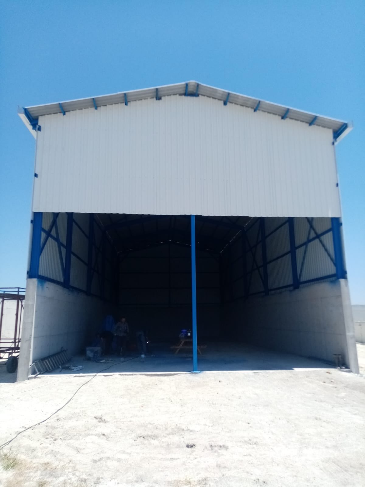 Mavi çelik kolon ve makaslar üzerine beyaz panel kaplı, ön cephesi açık geniş depo yapısı